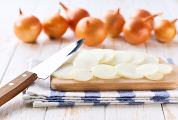 Sliced yellow onions in a cutting board on a light kitchen table.