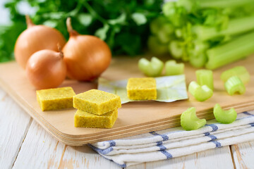 chicken bouillon cubes and fresh vegetables for soup on white wooden table, selective focus.