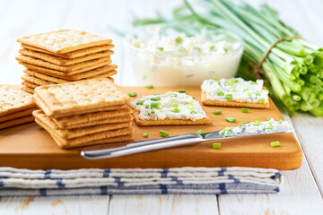 Biscuits with a cream cheese spread and freshly cut chives on a wooden cutting board, selective focus.