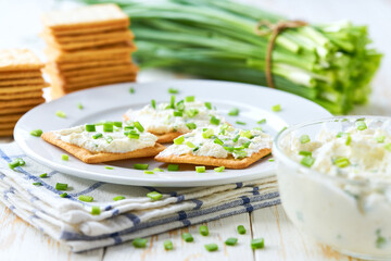 Fresh made snack, cream cheese with spring onions and crackers, on a wooden table, selective focus.