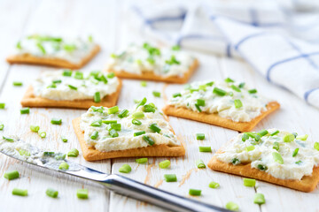 light snack of crackers with cream cheese and green onion on a blue napkin.