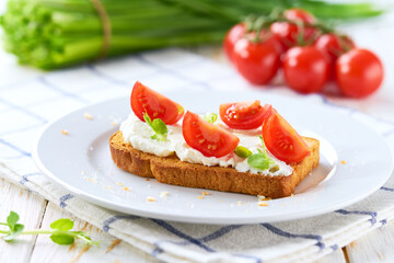 Sandwiches or toast with tomatoes cherry, cream cheese, olive oil and microgreen on a plate on white table.