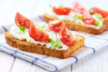 Healthy breakfast, bruschetta with ricotta cheese, and cherry tomatoes on a kitchen table.