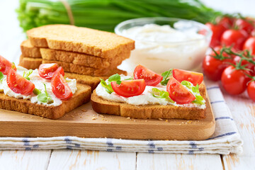 Healthy breakfast, bruschetta with ricotta cheese, and cherry tomatoes on a kitchen table.