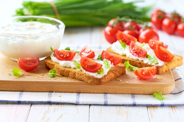Sandwiches or toast with tomatoes cherry, cream cheese, olive oil and microgreen on a plate on white table.