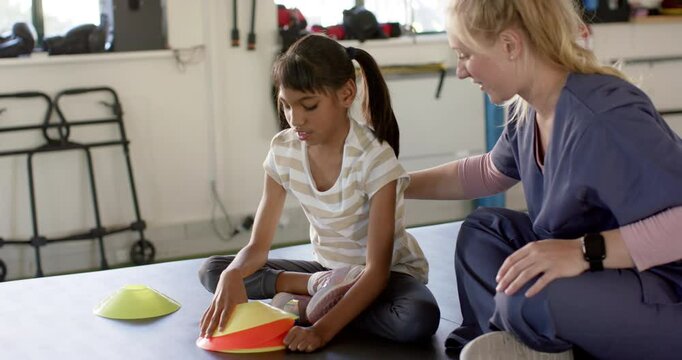 girl with cerebral palsy in disability rehab, playing with therapy cones, assisted by therapist