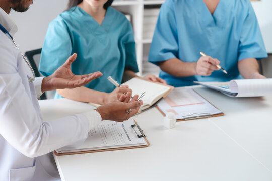 Two male doctors and a female nurse meet at a table in the hospital, collaborating on medical tasks, using laptops and computers, showcasing teamwork,and focusing on health,medicine,and patient care - Powered by Adobe