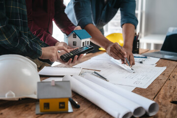 Two male engineers and a strong woman discuss blueprints and home design at a table. They work as a...