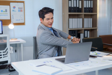 Naklejka premium Young businessman stretching arms at workplace after long working hours at computer