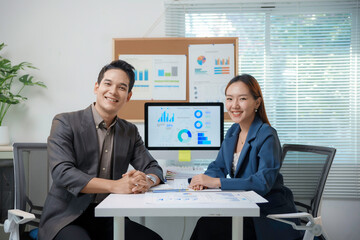 Asian business partners smiling and working together analyzing charts and graphs using computer at the office