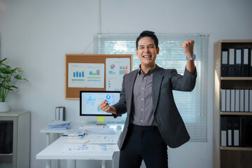 Excited Businessman Celebrating Success in Office with Charts and Graphs