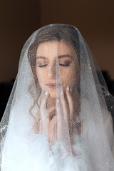 the bride stands behind a translucent veil that frames her face. She has long light brown hair...