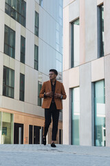 Young stylish businessman is walking along street on modern building background
