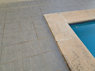 Fototapeta premium Minimalist poolside corner with gravel washed stone and concrete slabs, textured edge and grey detroit tiled flooring. Serene summery atmosphere for outdoor relaxation.