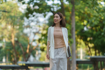 Businesswoman walking in a park holding a laptop and smiling