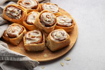 Delicious cinnamon rolls with white icing and almond flakes resting on wooden plate