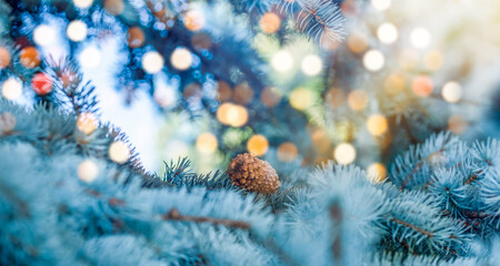 Christmas tree and lights bokeh around. New Year holidays concept with fir branches and pine cone on light background.
