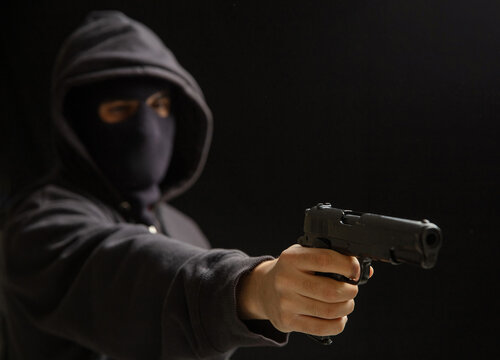 Robber with balaclava holding gun. Armed hooded killer Weapon, crime concept