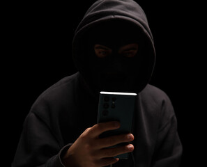 Hacker in black hood holding a cellphone, Scam cyber crime concept