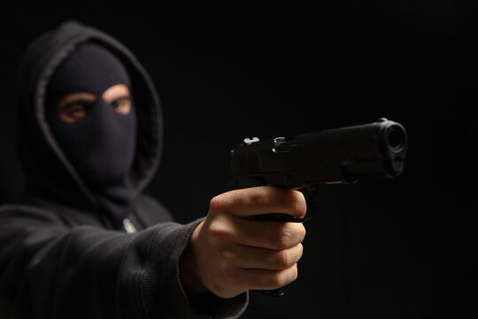 Robber with balaclava holding gun. Armed hooded killer Weapon, crime concept - Powered by Adobe