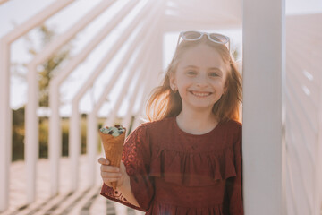 Happy little girl in sunglasses eats ice cream in summer in the park