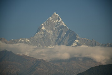 A stunning view of a towering snow-capped mountain peak surrounded by a layer of soft clouds. The...