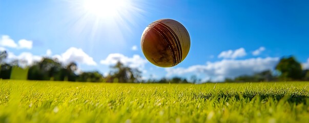 A cricket ball spinning in mid-air against the backdrop of a bright grassy field