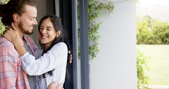 Biracial woman and Caucasian man laughing by window, embracing, copy space