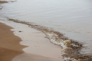 
a sandy beach with a line of small waves washing the shore.