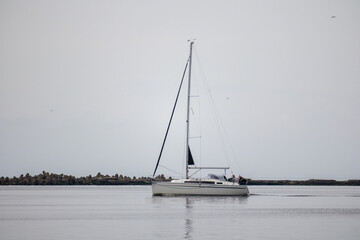 
a white yacht-type ship with its sails raised slowly floating in a calm sea.