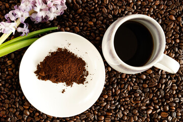 A white coffee cup filled with black coffee is placed on a bed of roasted coffee beans. 