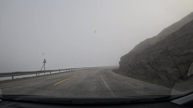 Driving through the tundra in northern Norway on E69 road. Surrounded by misty hills and rocky cliffs, creating a dramatic and serene landscape.