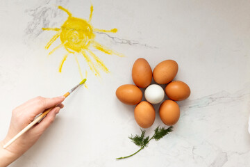 A skillful hand expertly paints the shining sun with beautiful multicolored eggs forming a bright...