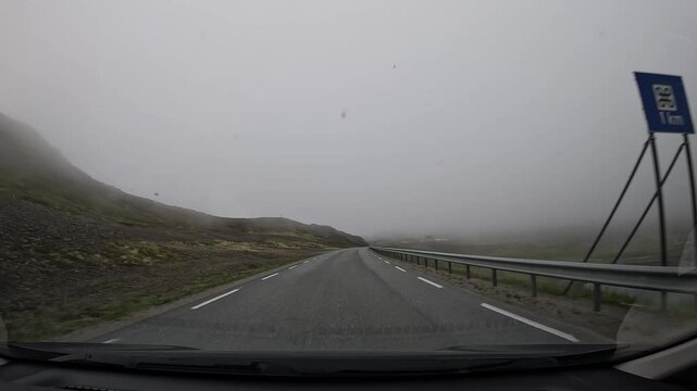 Driving through the tundra in northern Norway on E69 road. Misty views of grassy slopes, hills, scattered houses, and a small lake create a serene and picturesque scene.