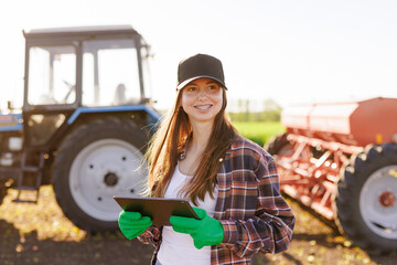 a girl agronomist with a tablet manages agribusiness against the background of a tractor, modern...