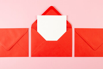 Top view of red envelopes, white card on pink background. Post flat lay. Copy space.