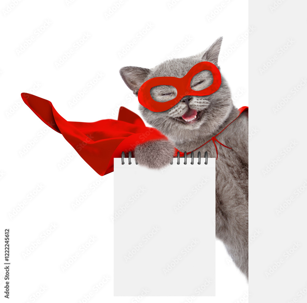 Poster happy cat wearing superhero costume shows blank notepad in it paw and looks from behind blank white 