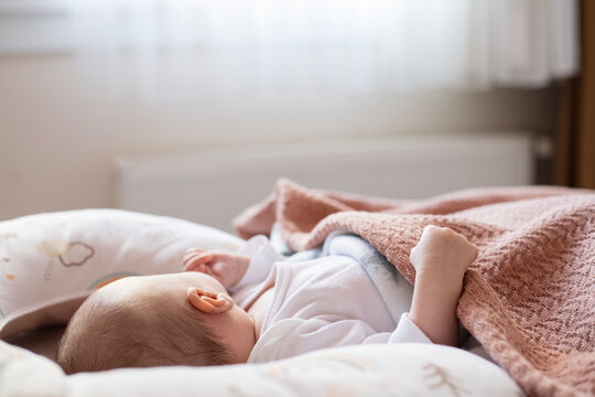 Infant in white bodysuit lying on side in comfortable bed on white sheet. Back view. Closeup. Baby correct sleeping position.