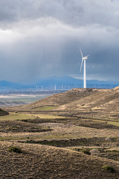 A solitary wind turbine towers against dark, brooding clouds, highlighting the contrast between innovation and the raw power of nature in a dramatic landscape in Zaragoza Spain