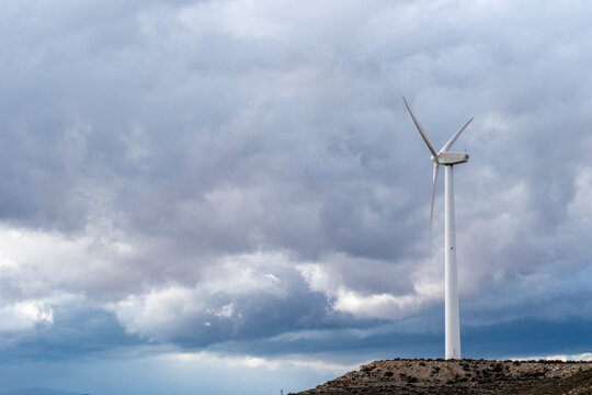 A single wind turbine stands prominently on rolling hills under an expanse of moody clouds, symbolizing isolation and innovation in renewable energy in Zaragoza Spain