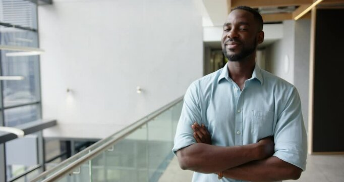 Smiling businessman standing confidently with arms crossed in modern office hallway, copy space