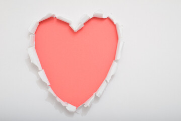 A heart-shaped cutout is formed by tearing white paper to reveal a coral-colored surface underneath
