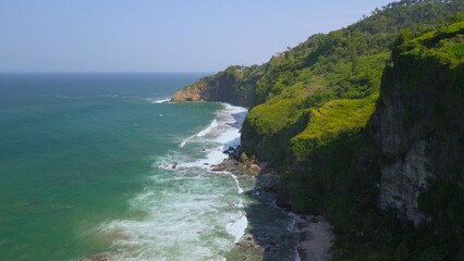  A man standing in the top of hill in coastline with hills, cliffs, trees, beach sand and waves from the sea and ocean at Menganti Beach, Kebumen, Central Java, Indonesia
