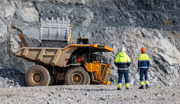 Team work engineers control loading of gold ore by excavator into large quarry yellow truck. Concept open pit mine industry.
