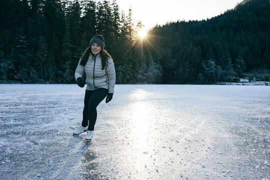 Ice skating on a frozen lake under soft sunlight and forest views.