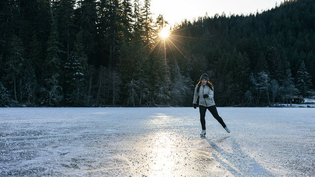 Woman ice skating on a frozen lake surrounded by a winter forest
