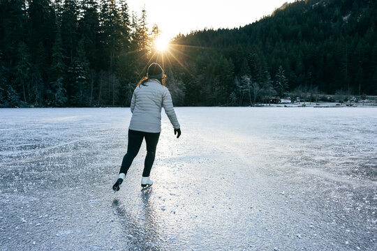 Woman skating on a frozen lake surrounded by a winter forest