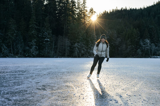 Female ice skater gliding on a reflective frozen lake at sunset.