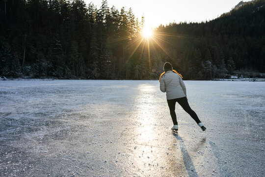 Ice skater on a peaceful lake under soft sunlight and forest views