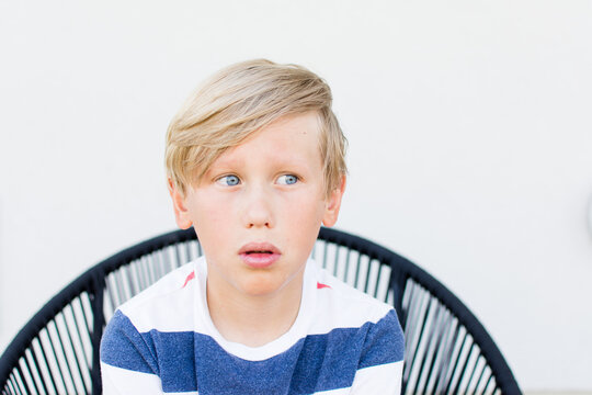A thoughtful blonde boy sits in modern chair, white background